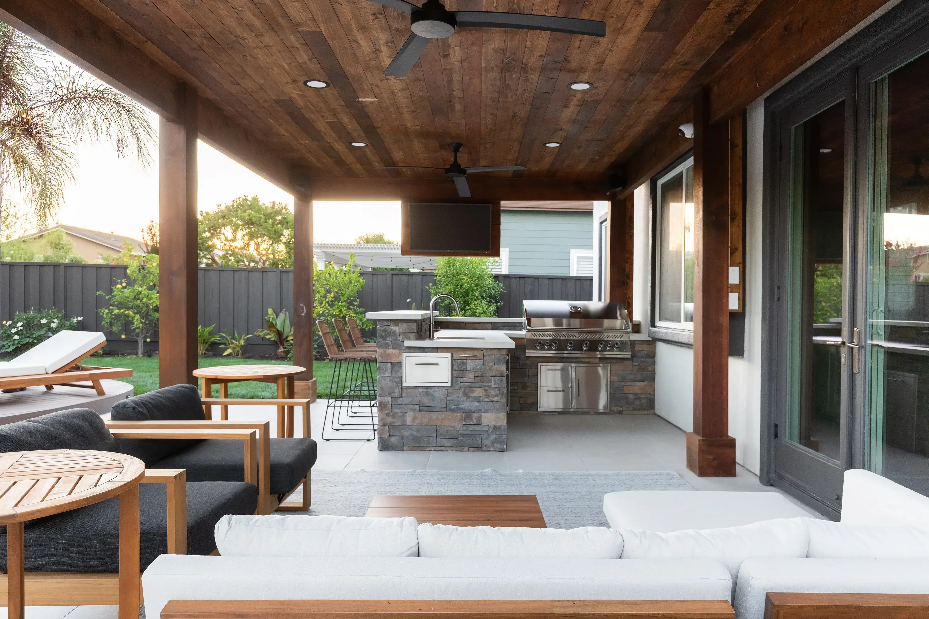 Covered patio with wood ceiling, stacked stone outdoor kitchen, stainless steel grill, and lounge seating