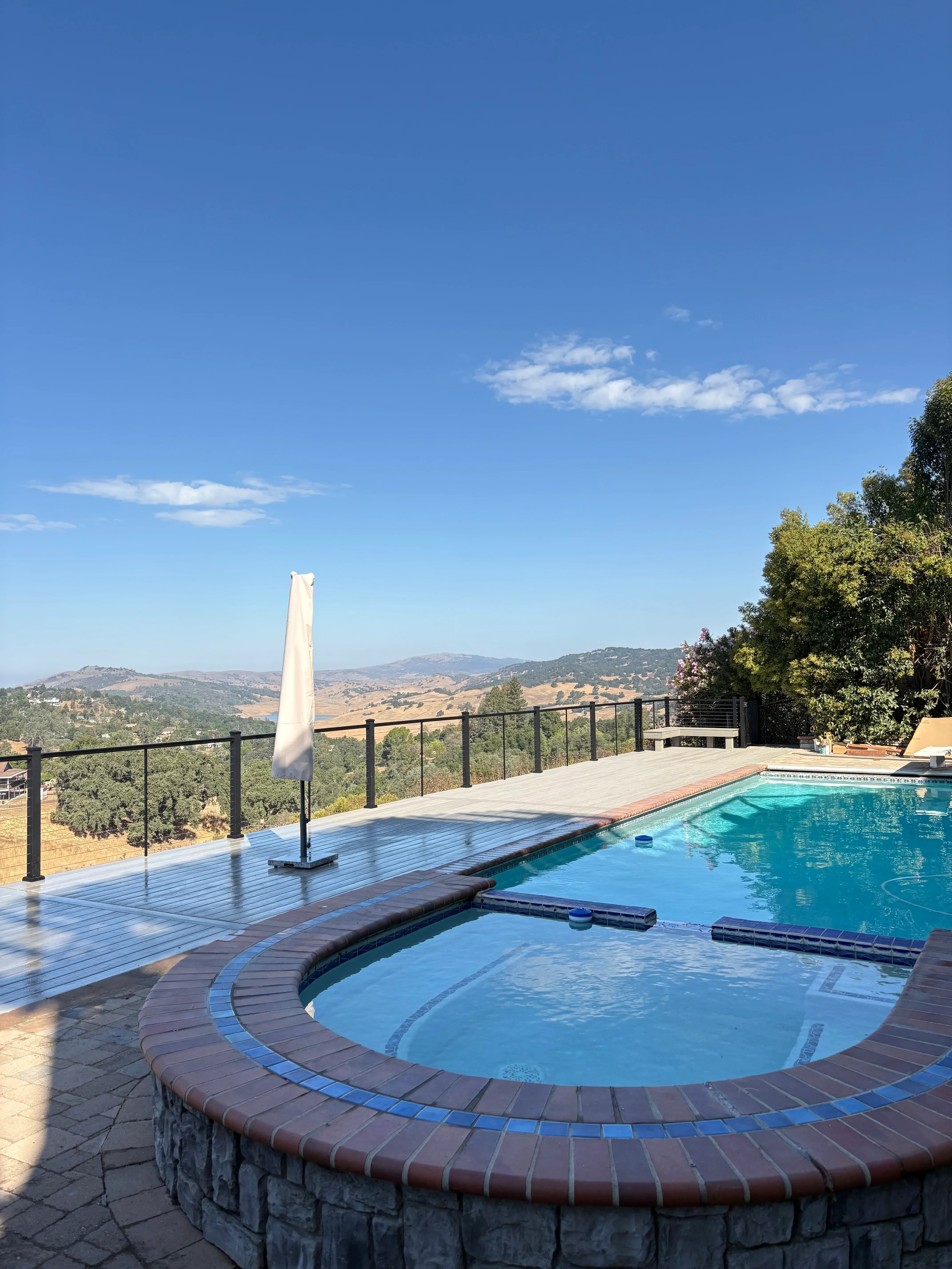 Pool and spa deck with curved brick borders, composite decking, and cable railing overlooking rolling hills