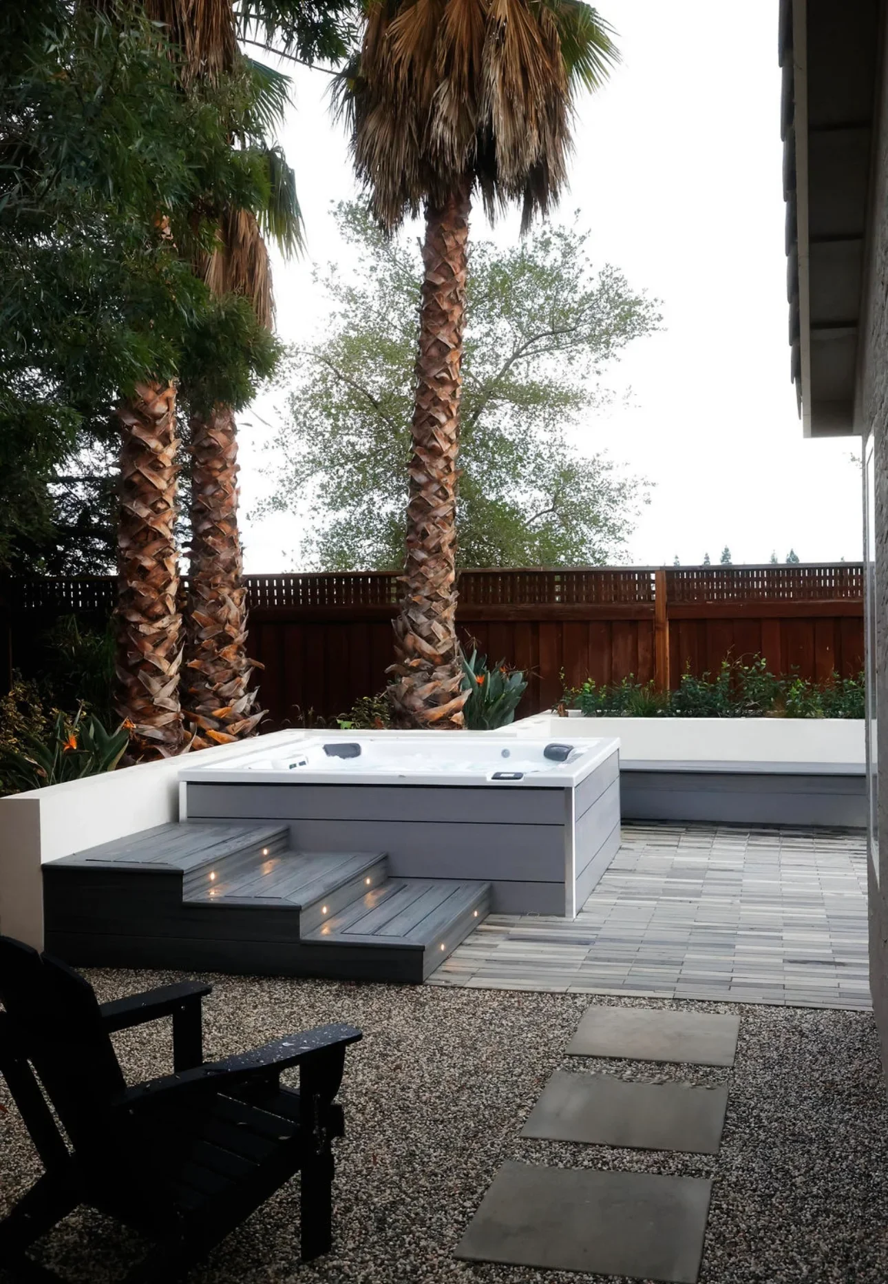 Modern hot tub deck with LED-lit composite steps, white bench seating, and gray decking in residential backyard
