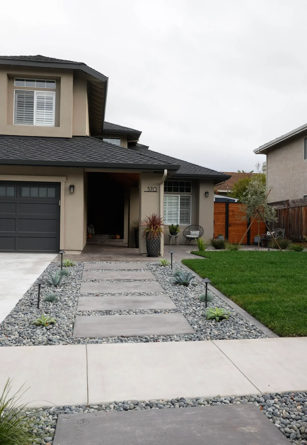 Modern home front yard with gray stepping stone pathway bordered by river rock and low-water plants