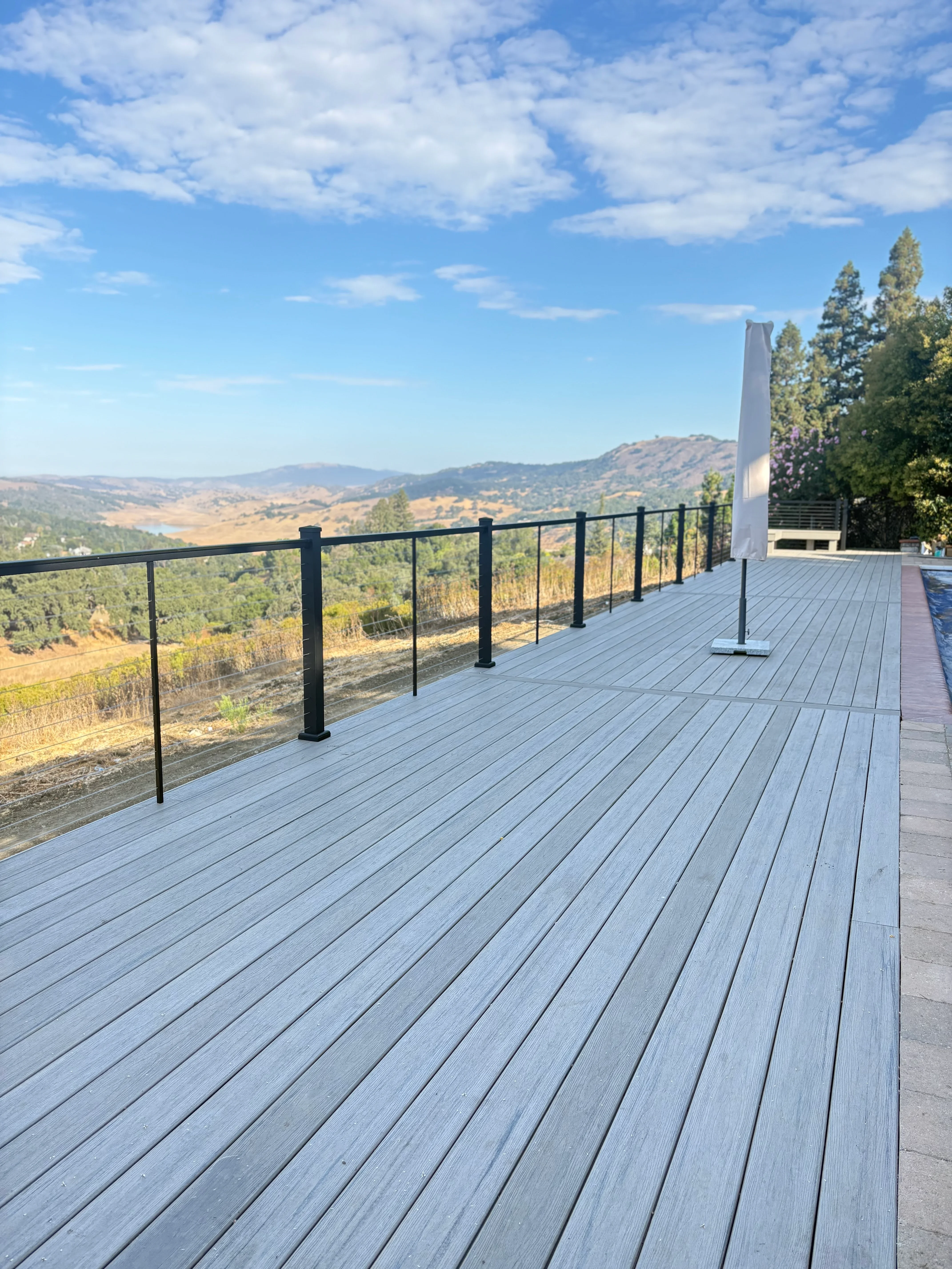 Gray composite deck with black glass railing overlooking Morgan Hill valley landscape