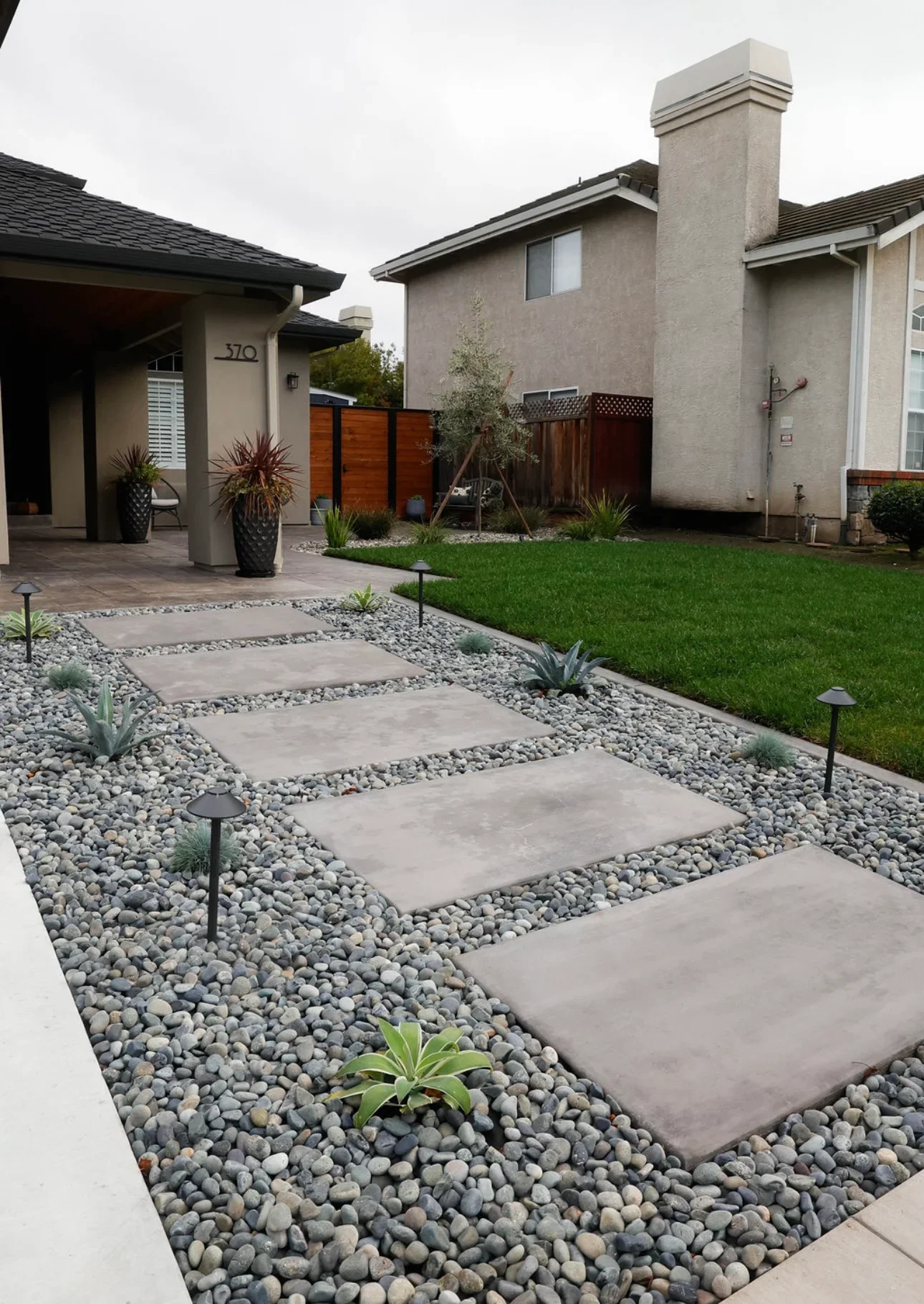 Modern backyard with concrete stepping stones, river rock, lawn, and wooden fence