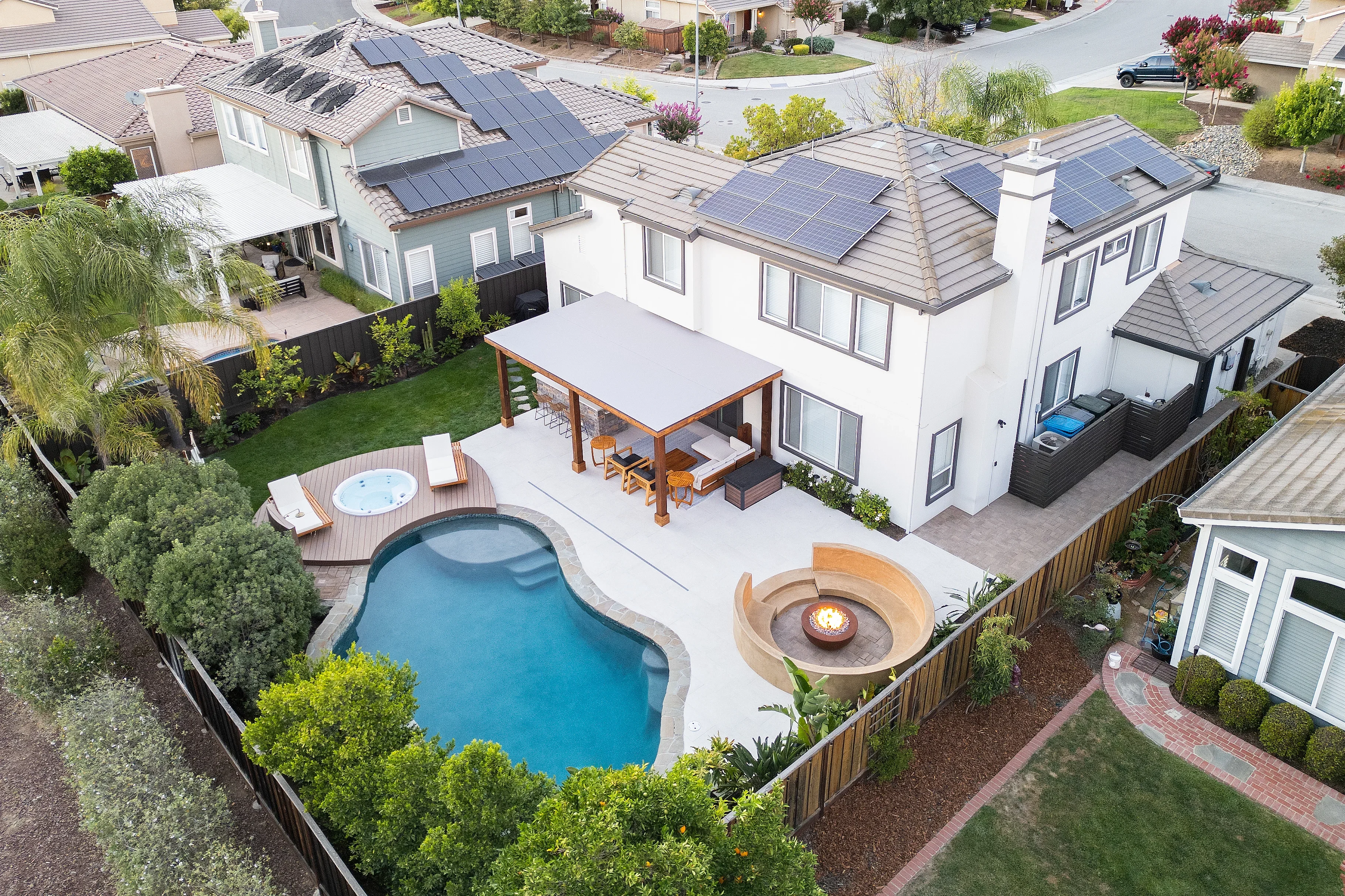 Aerial view of pool, concrete patio, pergola, and fire pit in residential backyard