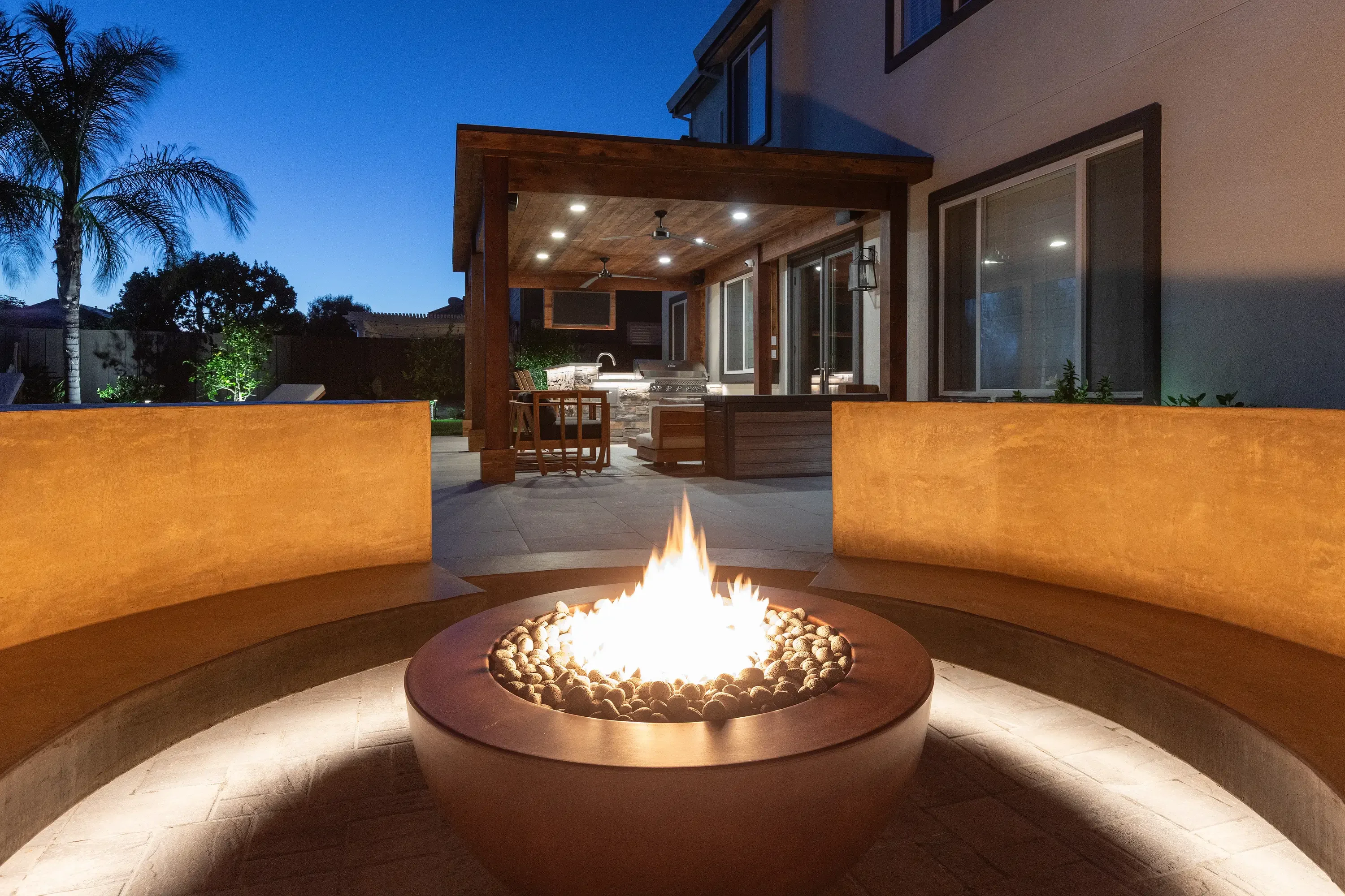 Concrete fire pit with curved seating walls, LED lighting, and stainless steel ring on patio