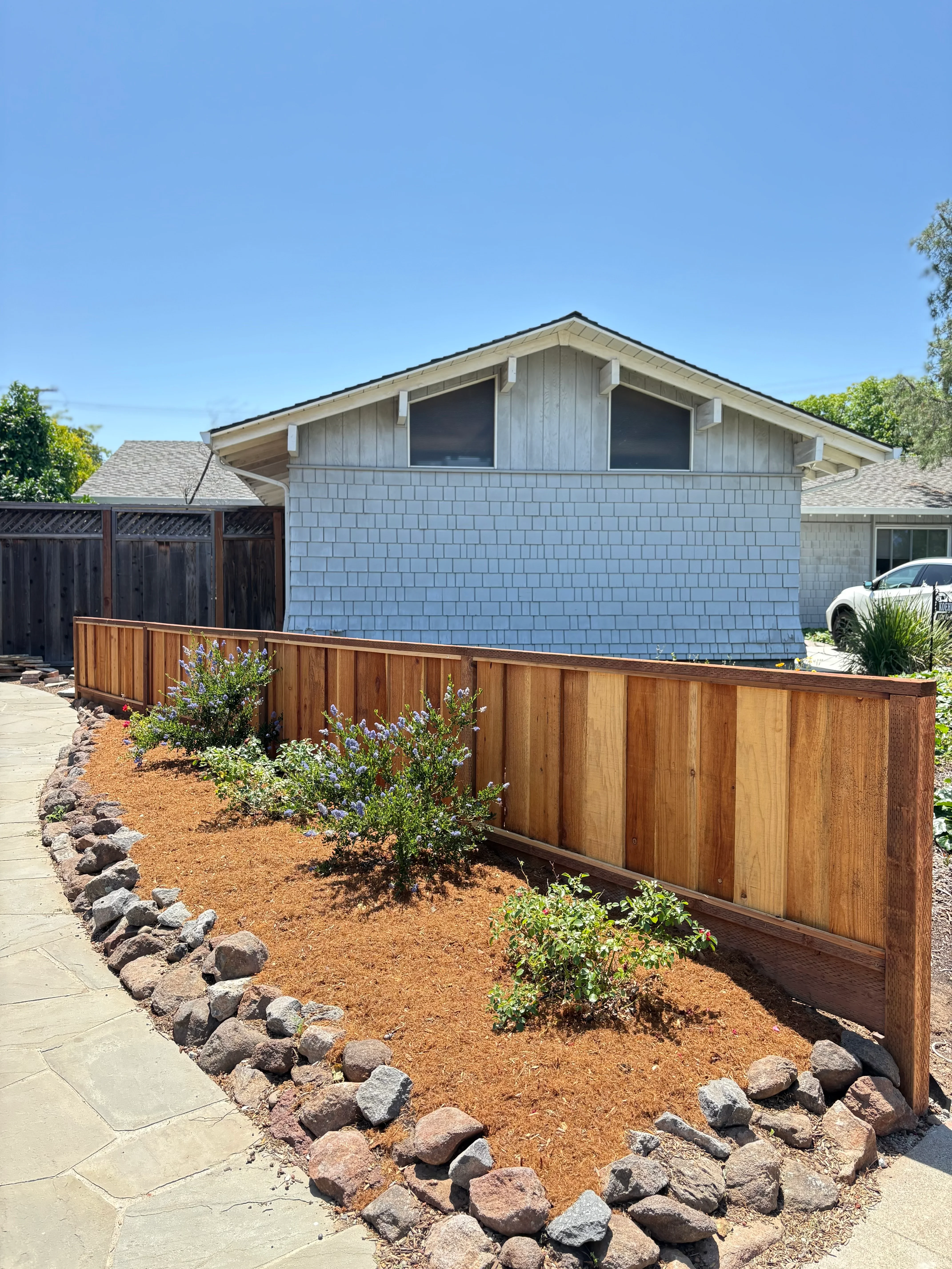 Modern home with new wood fence, mulched planting beds, and rock edging landscaping