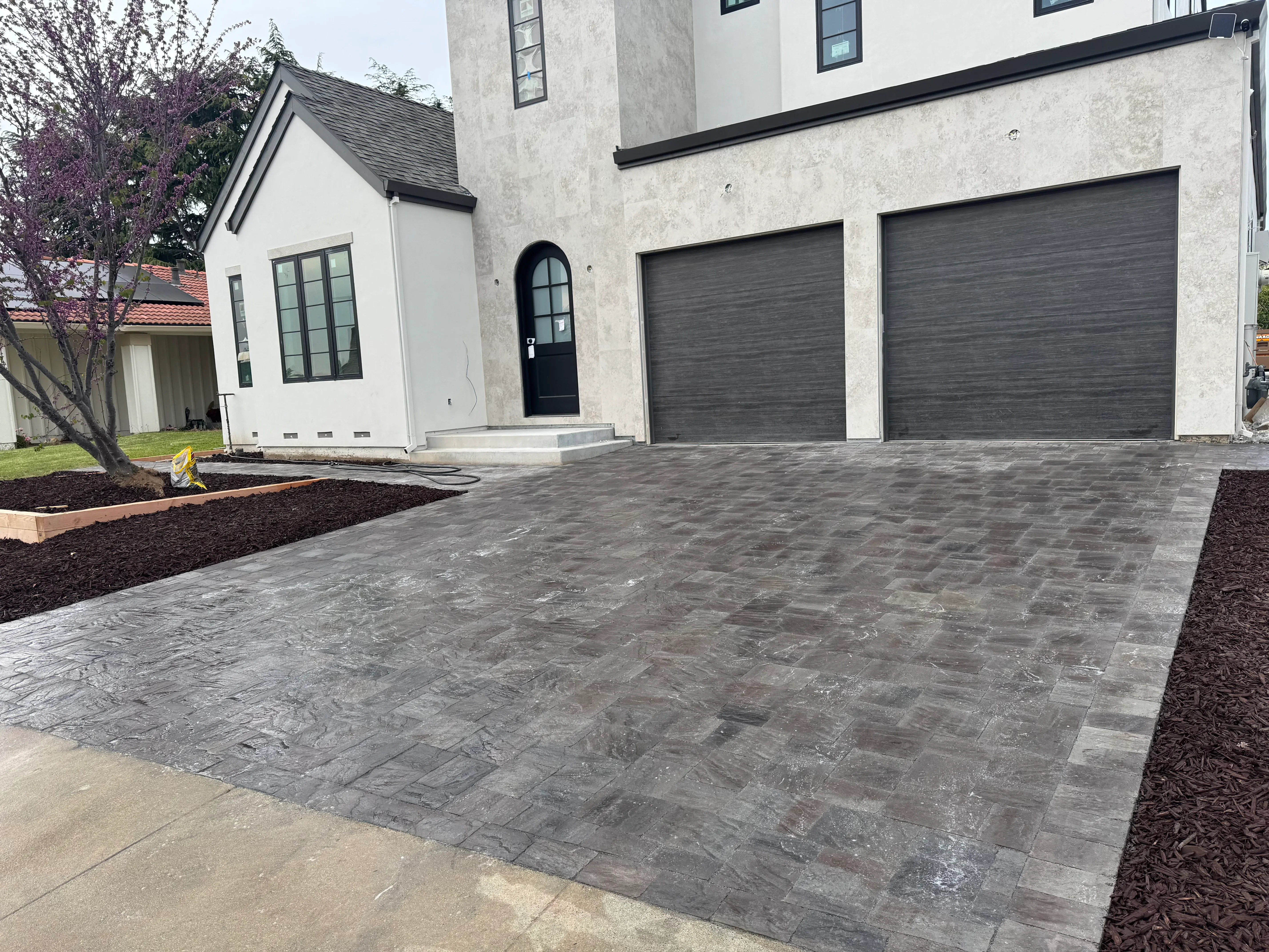 Gray herringbone paver driveway with black garage doors and landscaped beds