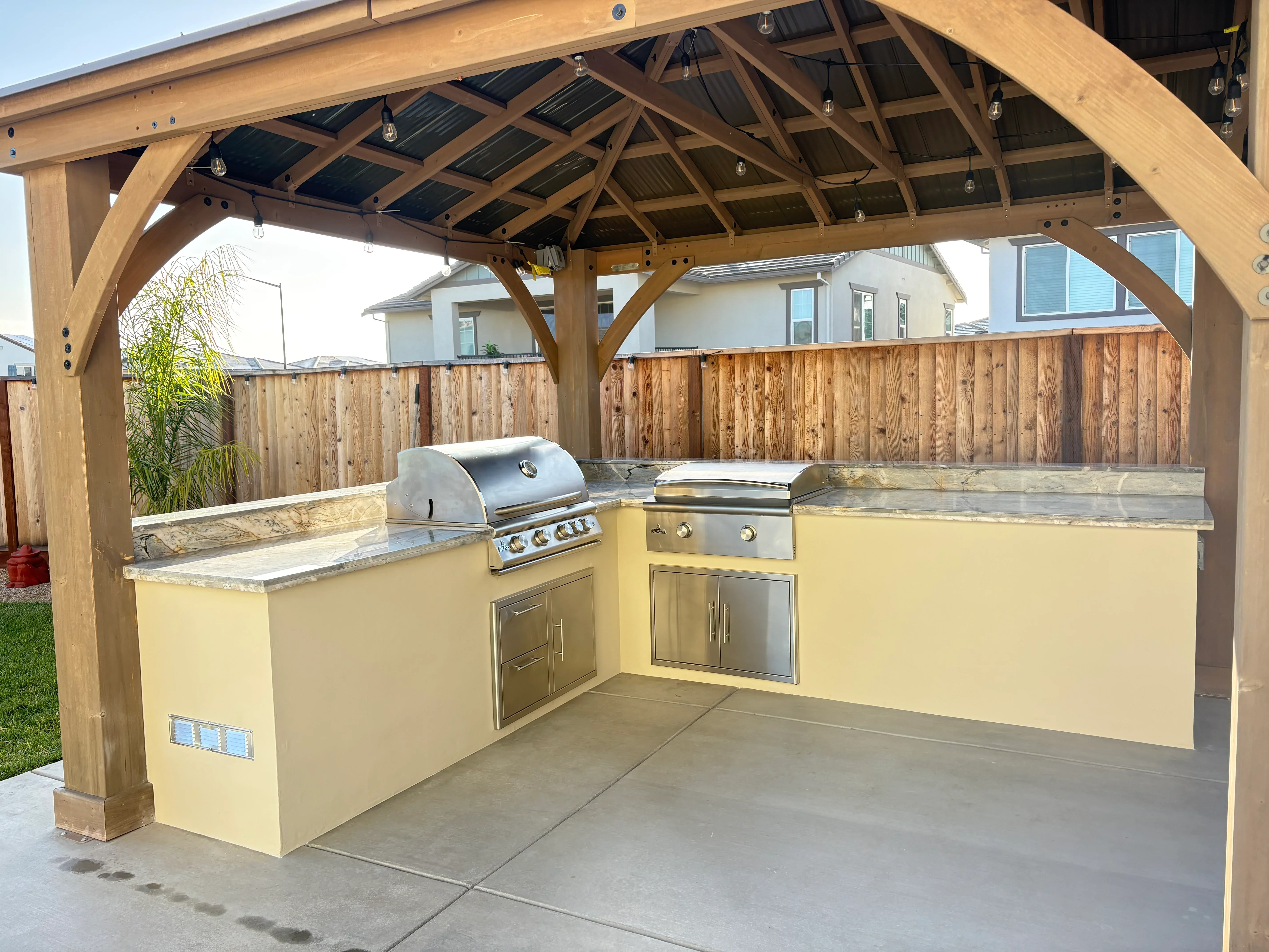 Outdoor kitchen with yellow stucco cabinetry, stainless steel appliances, and wooden pergola overhead