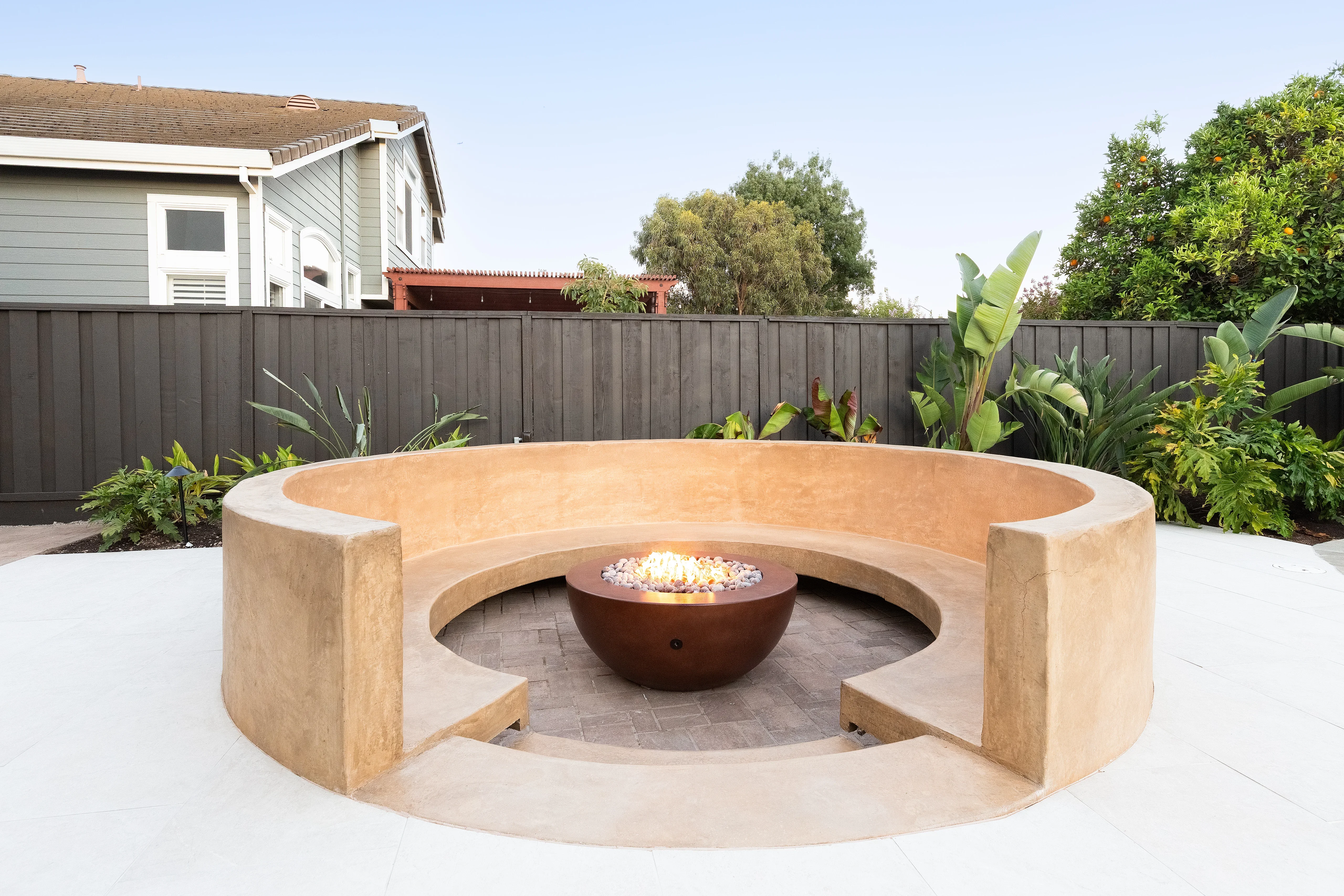 Curved concrete bench seating surrounding a metal fire bowl with decorative stone base