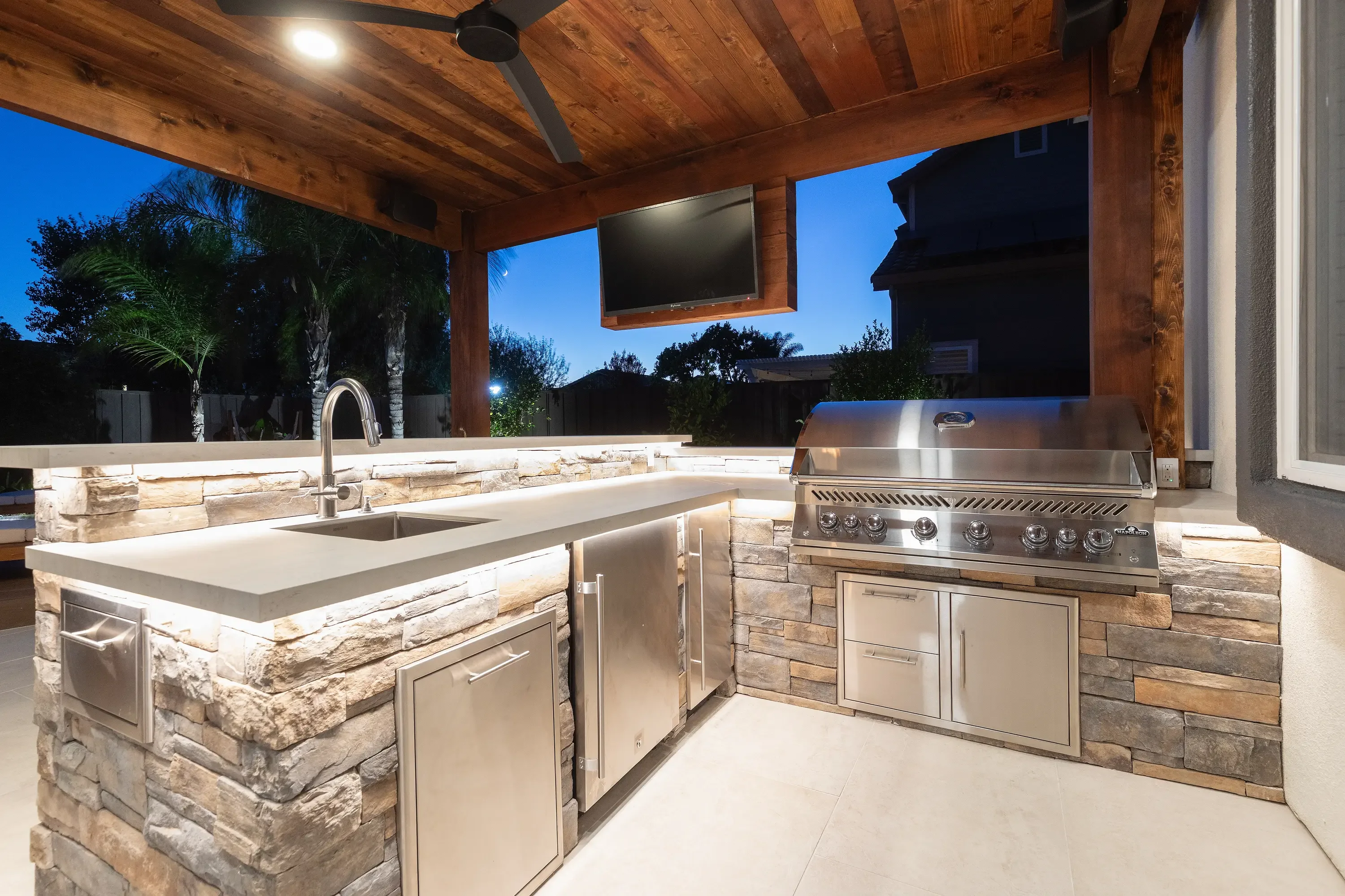 Outdoor kitchen with stone veneer, quartz counters, stainless steel grill, and timber pergola