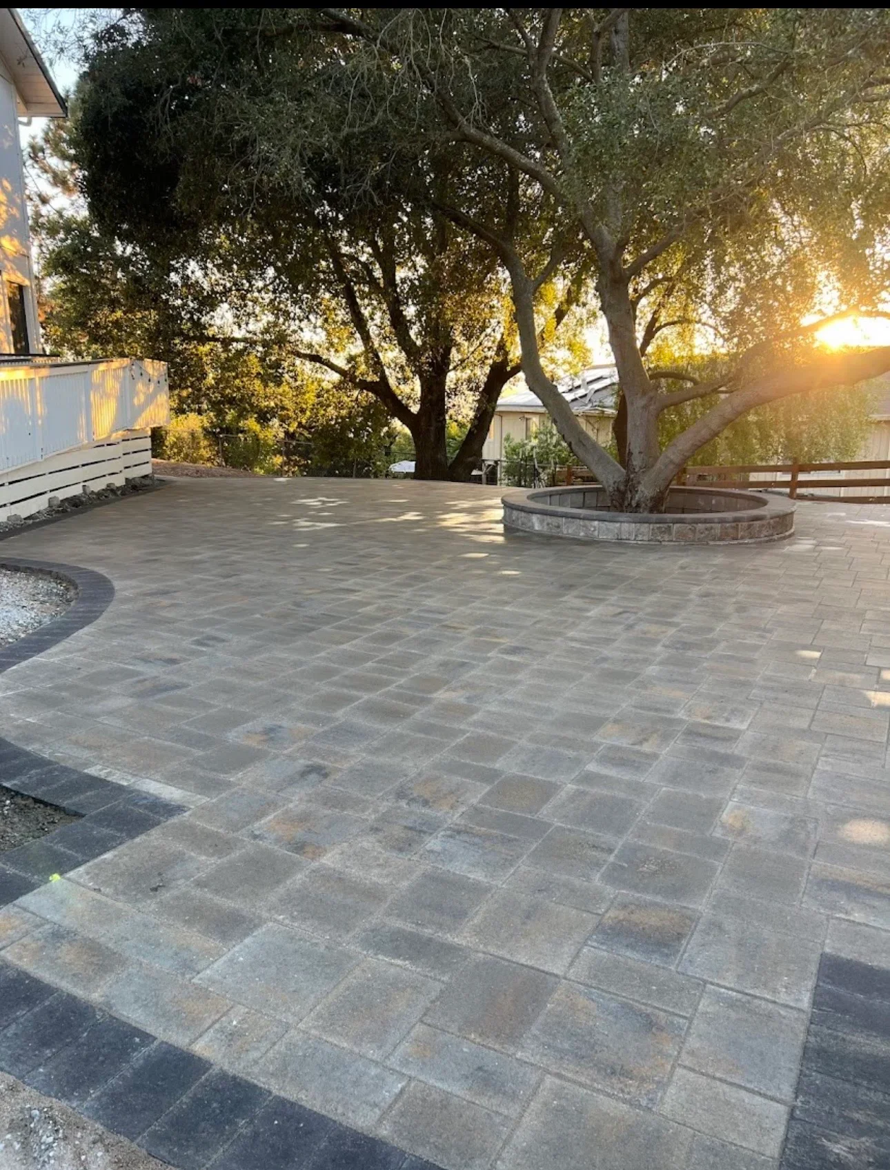 Gray stone paver patio with circular tree surround and wooden fence at sunset