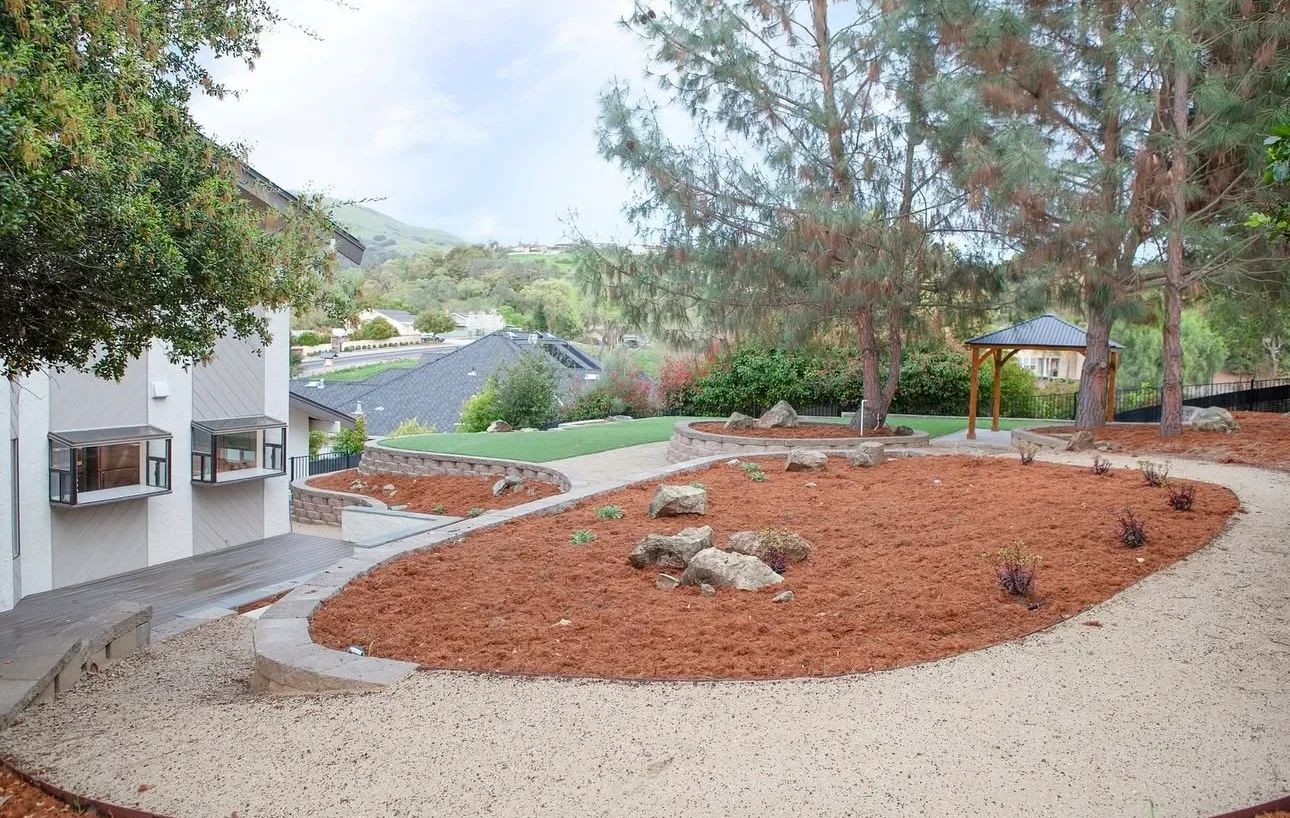 Modern hillside estate landscape with mulched beds, boulders, mature trees, and valley views