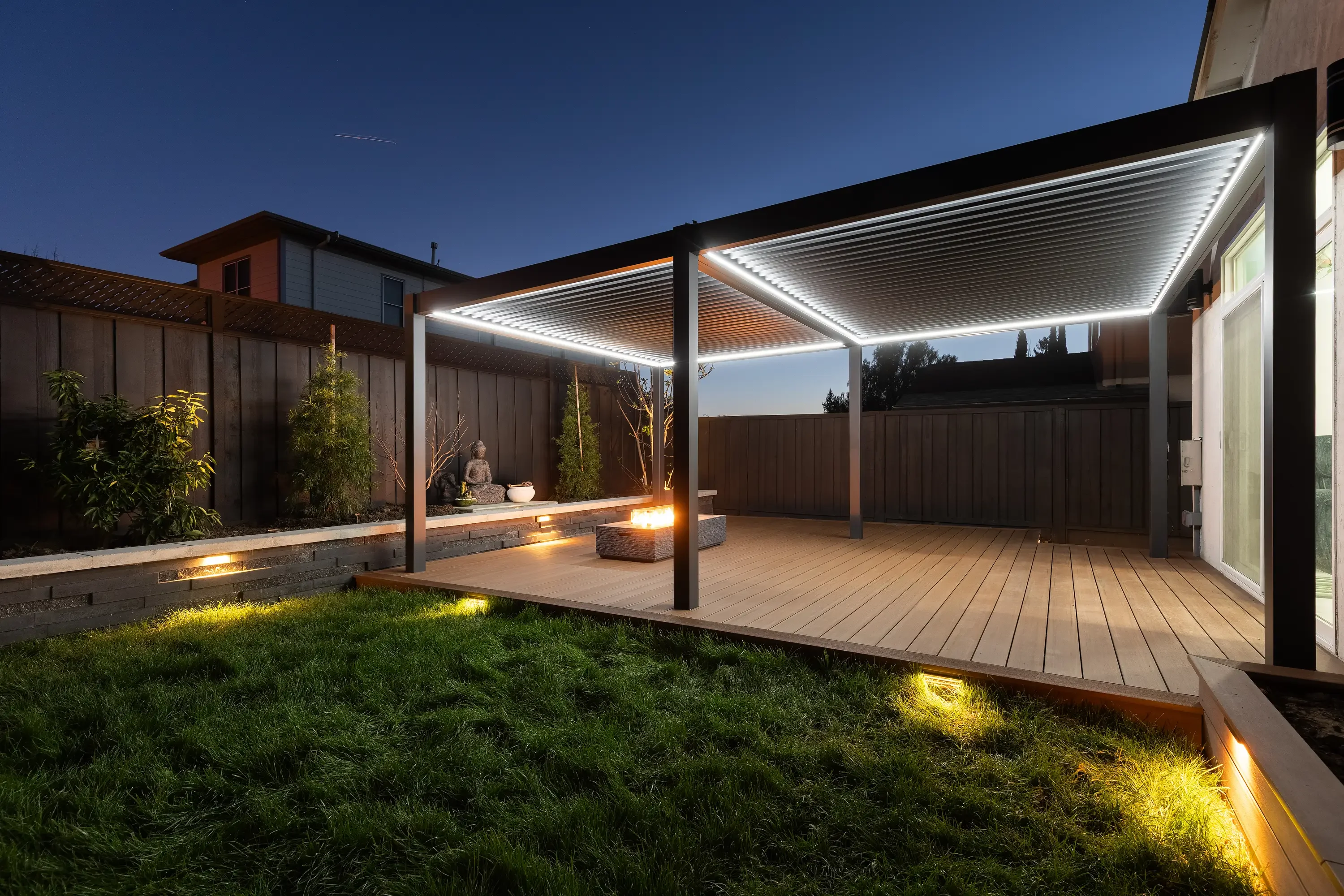 Modern backyard deck at dusk with LED-lit pergola, composite decking, and landscape lighting