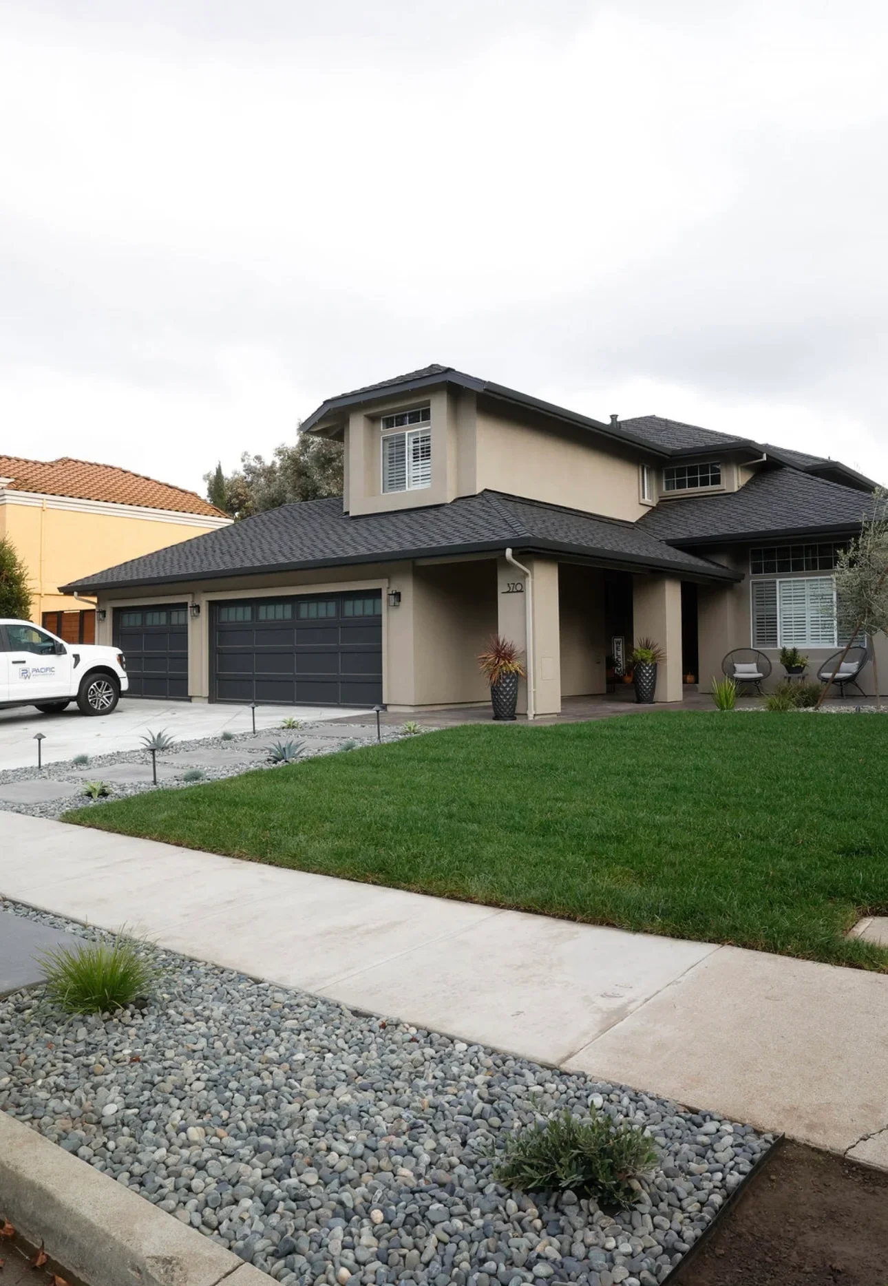 Modern home with manicured lawn, river rock landscaping, and concrete walkway