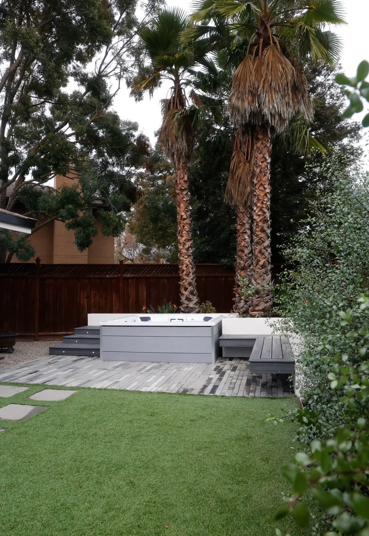 Modern spa deck with composite boards, built-in seating, and mature palms in residential backyard