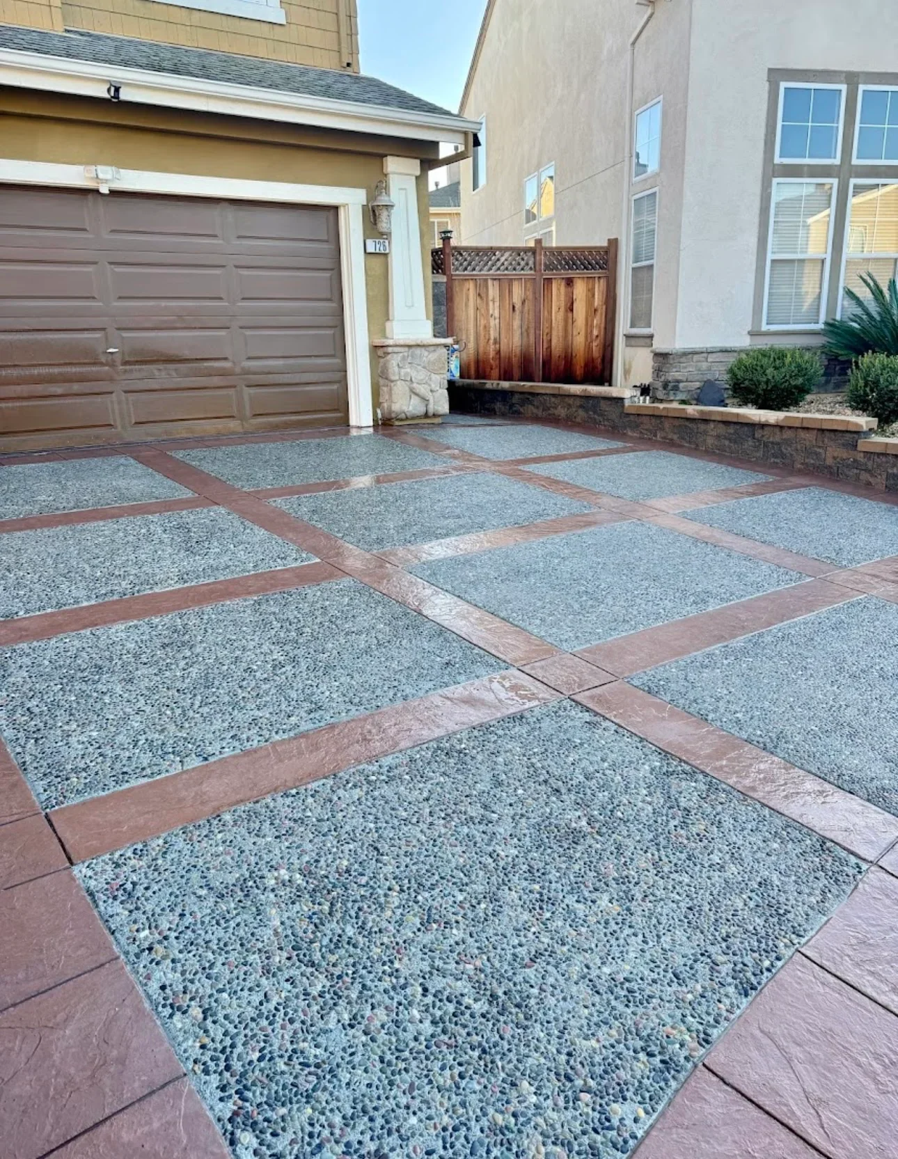 Residential driveway with gray permeable pavers and red-brown concrete border strips in grid pattern