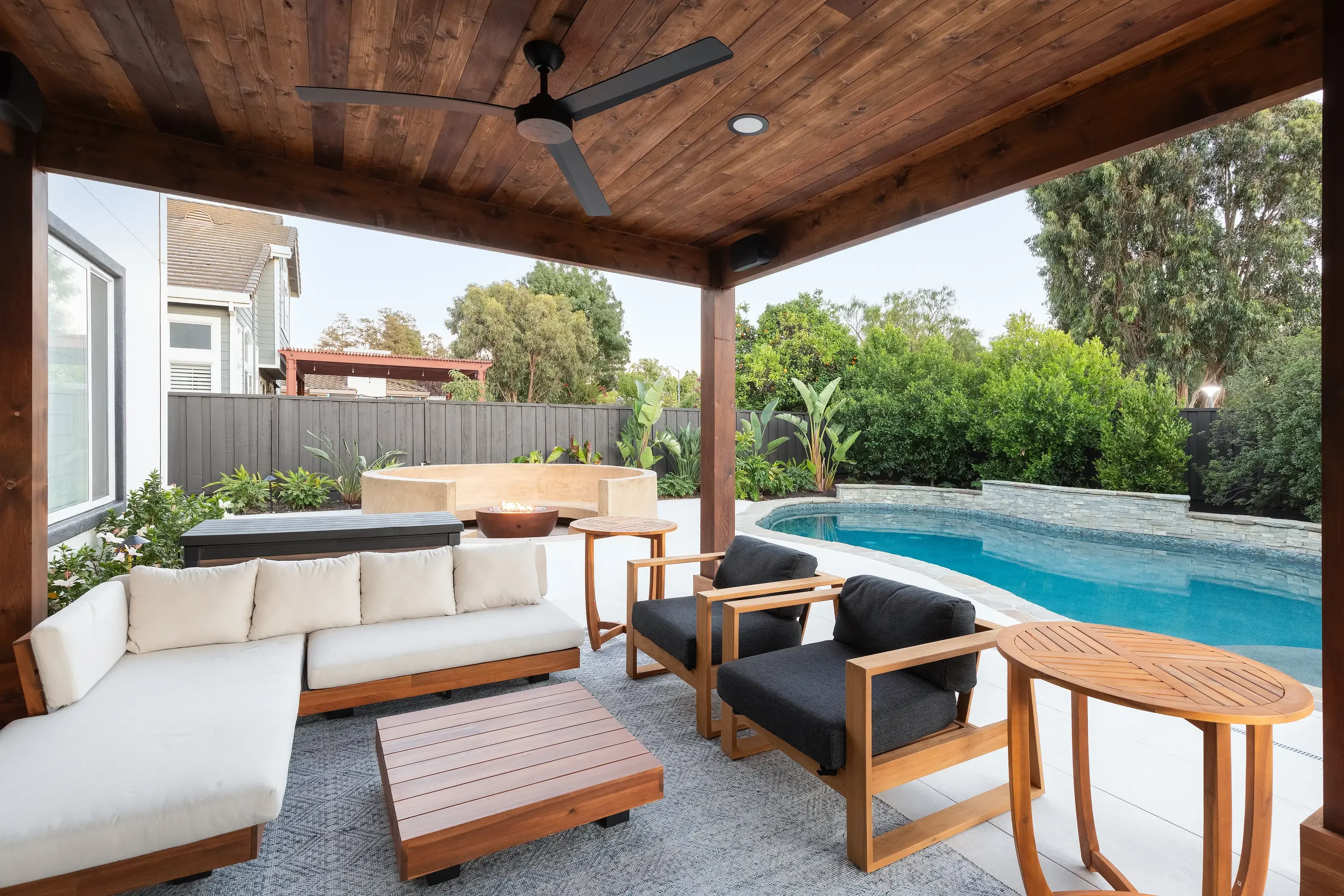 Wood pergola with ceiling fan over patio seating area adjacent to pool and spa