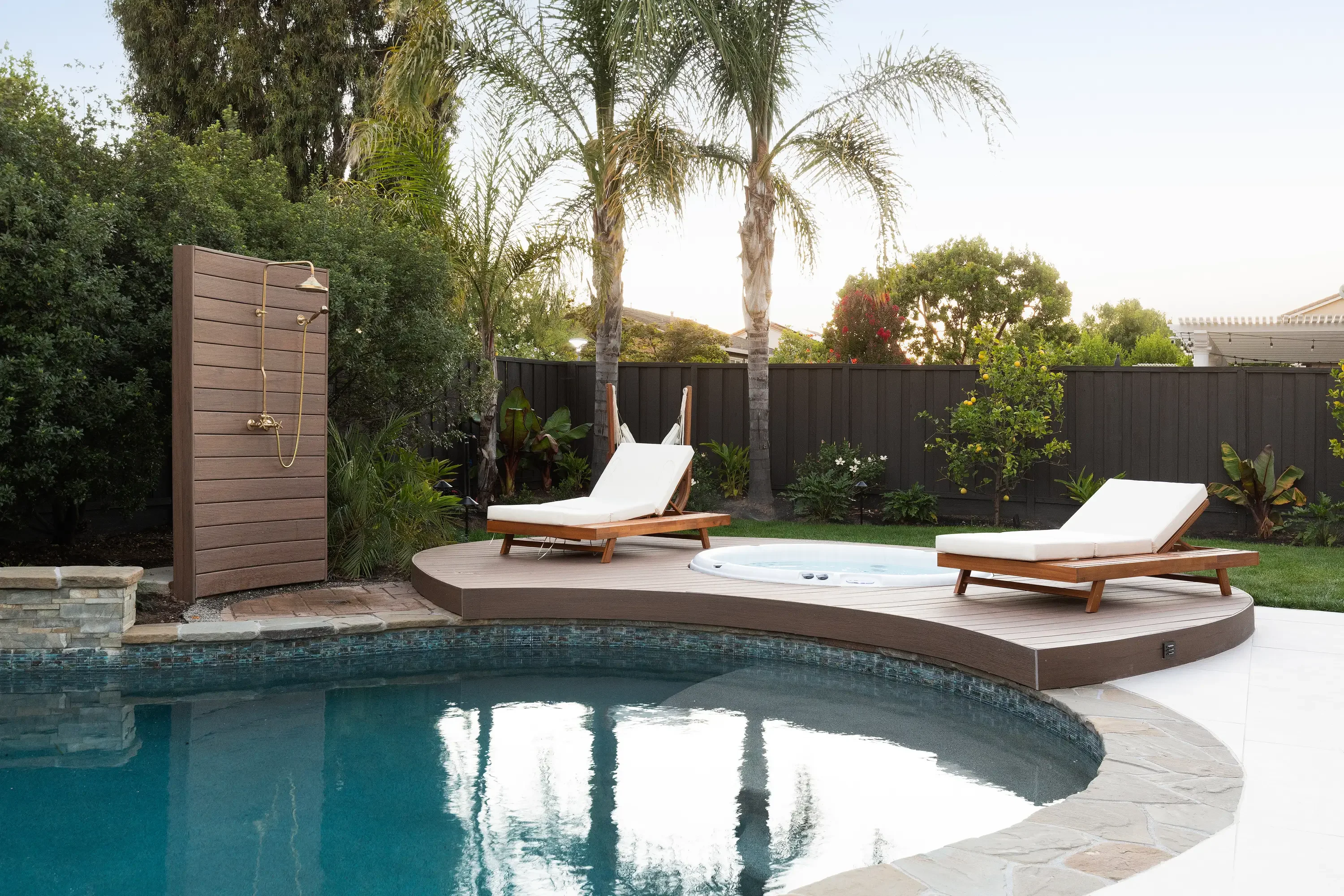 Curved composite pool deck with outdoor shower enclosure, spa, and lounge seating area