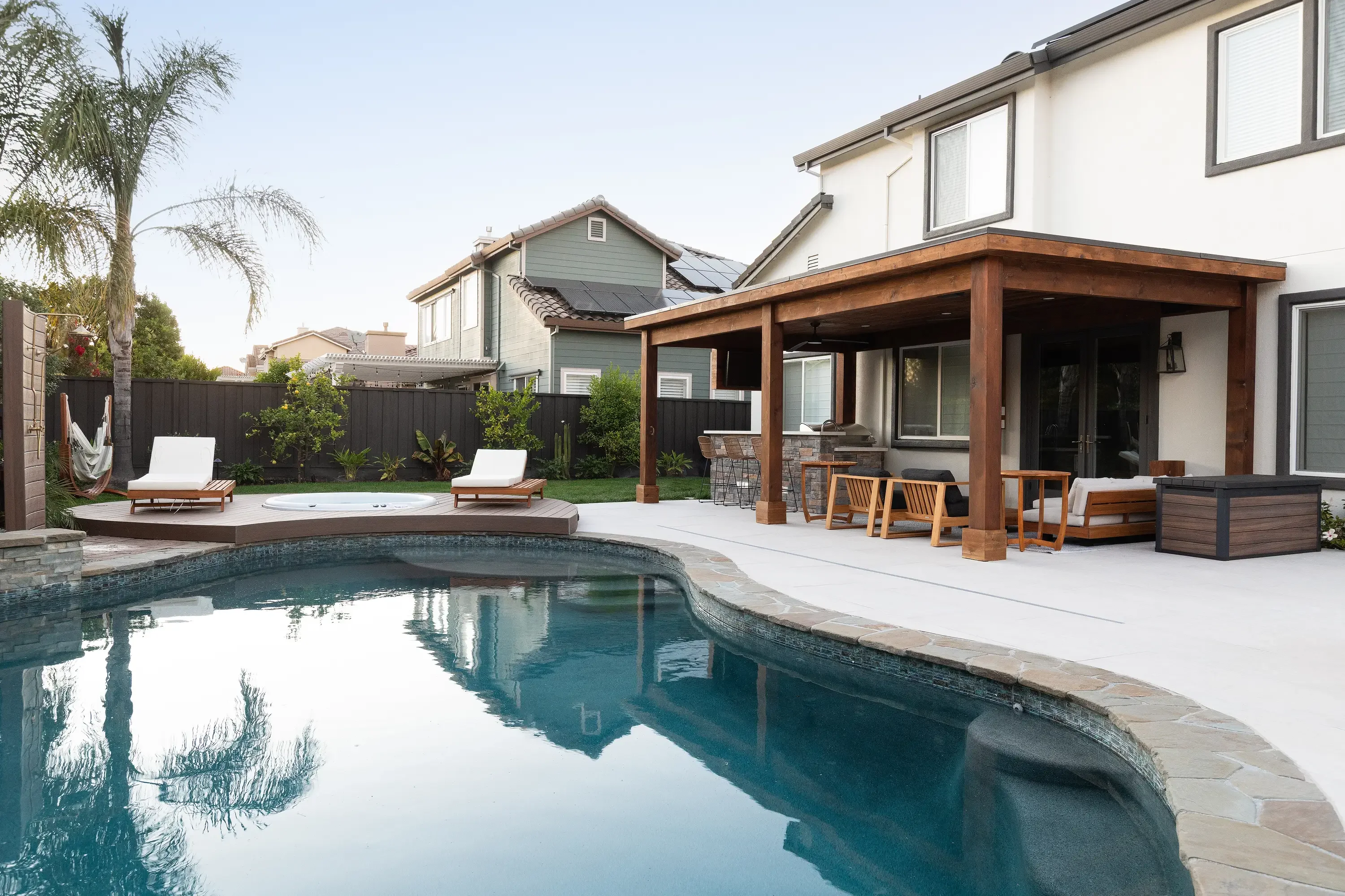 Pool with stone coping, concrete patio, timber pergola, and integrated landscape planting