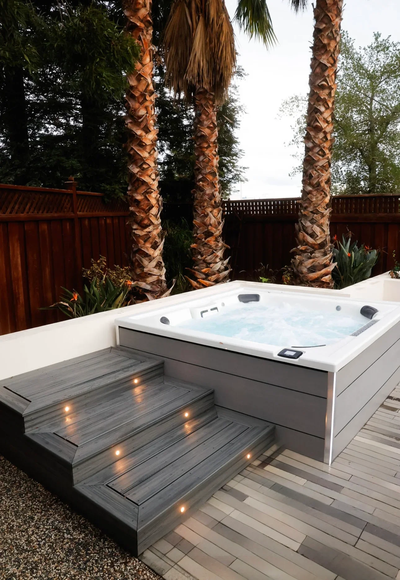 Elevated hot tub on composite deck with lit steps and palm trees