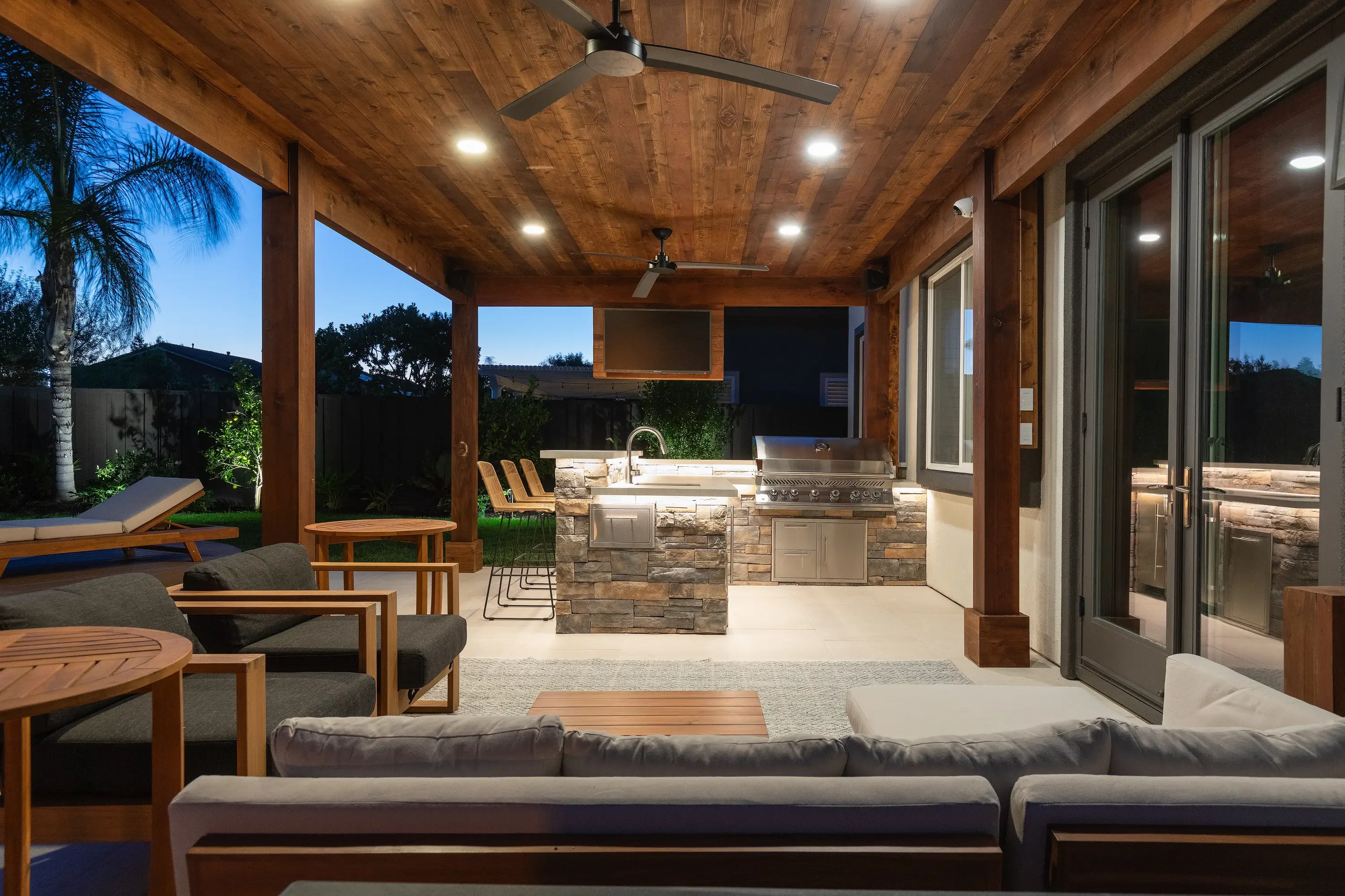 Covered patio with wood ceiling, stainless steel grill, stacked stone kitchen island, and seating area