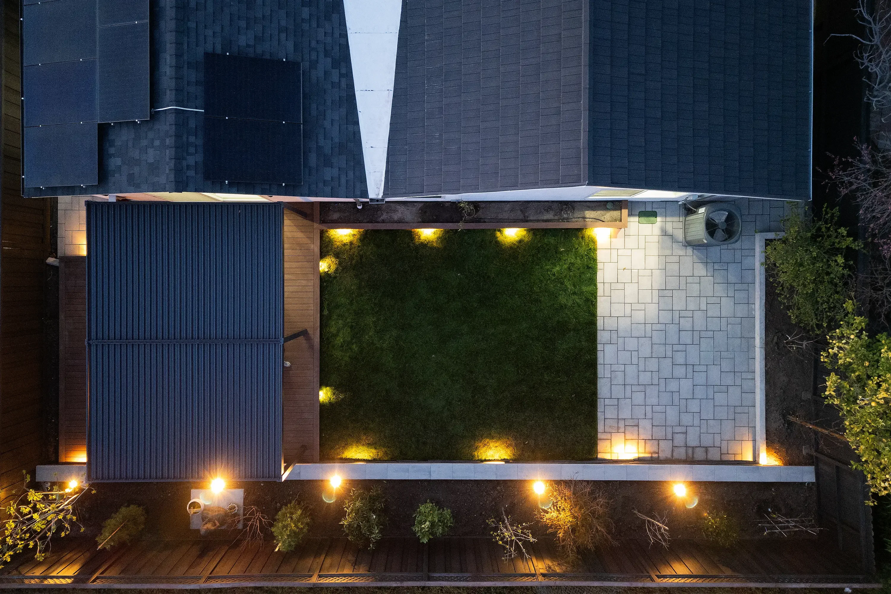 Modern courtyard with illuminated green living wall, geometric pavers, and landscape lighting at dusk