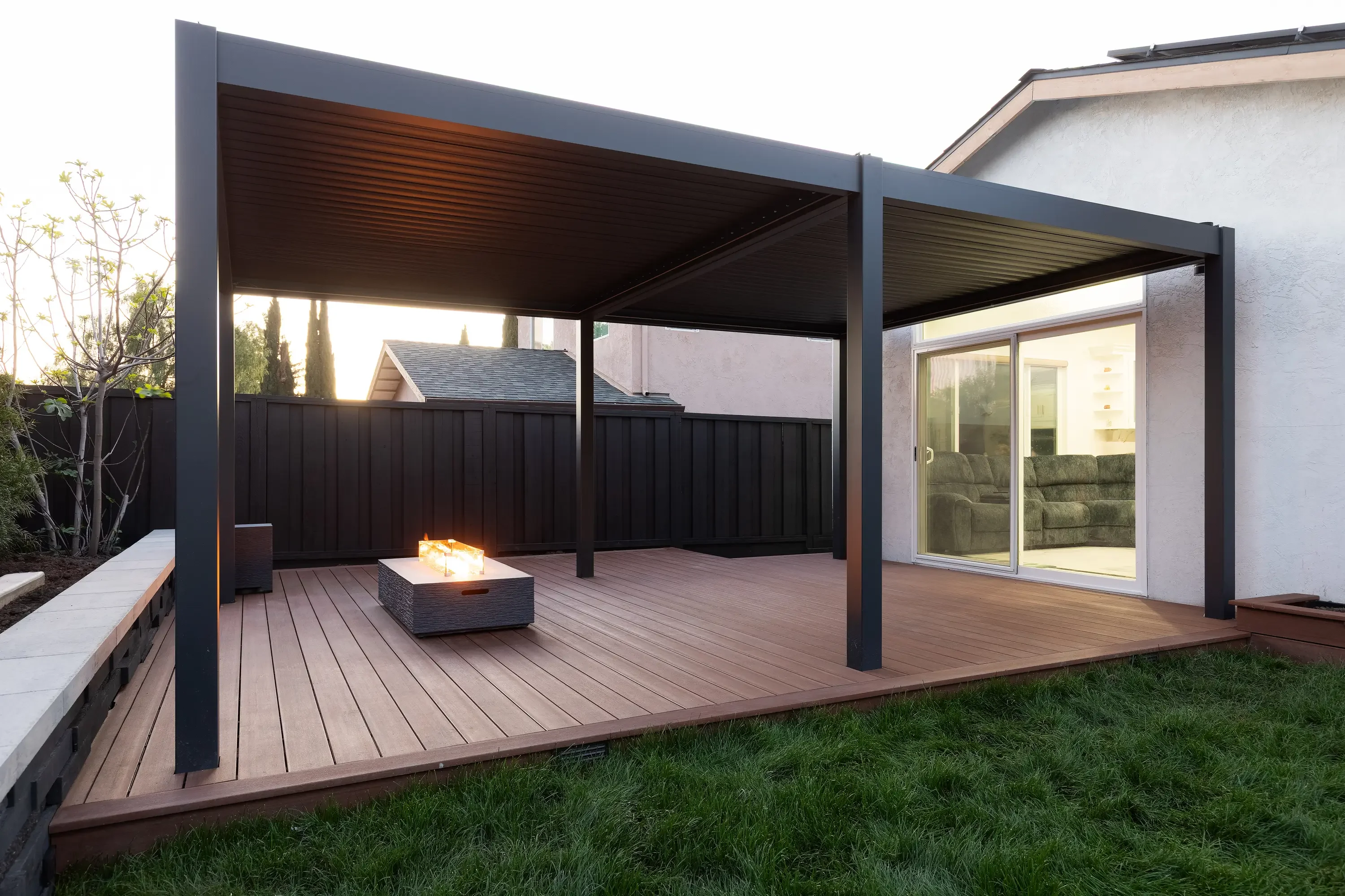 A custom wood pergola installed in a Morgan Hill backyard, with open lattice beams casting filtered shade over a concrete patio. The structure is attached to the rear of a single-story home with a landscaped yard visible in the background.